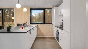 Eine moderne Küche mit einer großen Kochinsel, Holzpaneelen und Blick auf Bäume durch die Fenster.