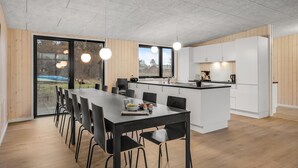 Eine moderne Küche mit einer zentralen Kochinsel, einem Essbereich mit einem langen Tisch und Stühlen sowie Blick durch große Fenster.