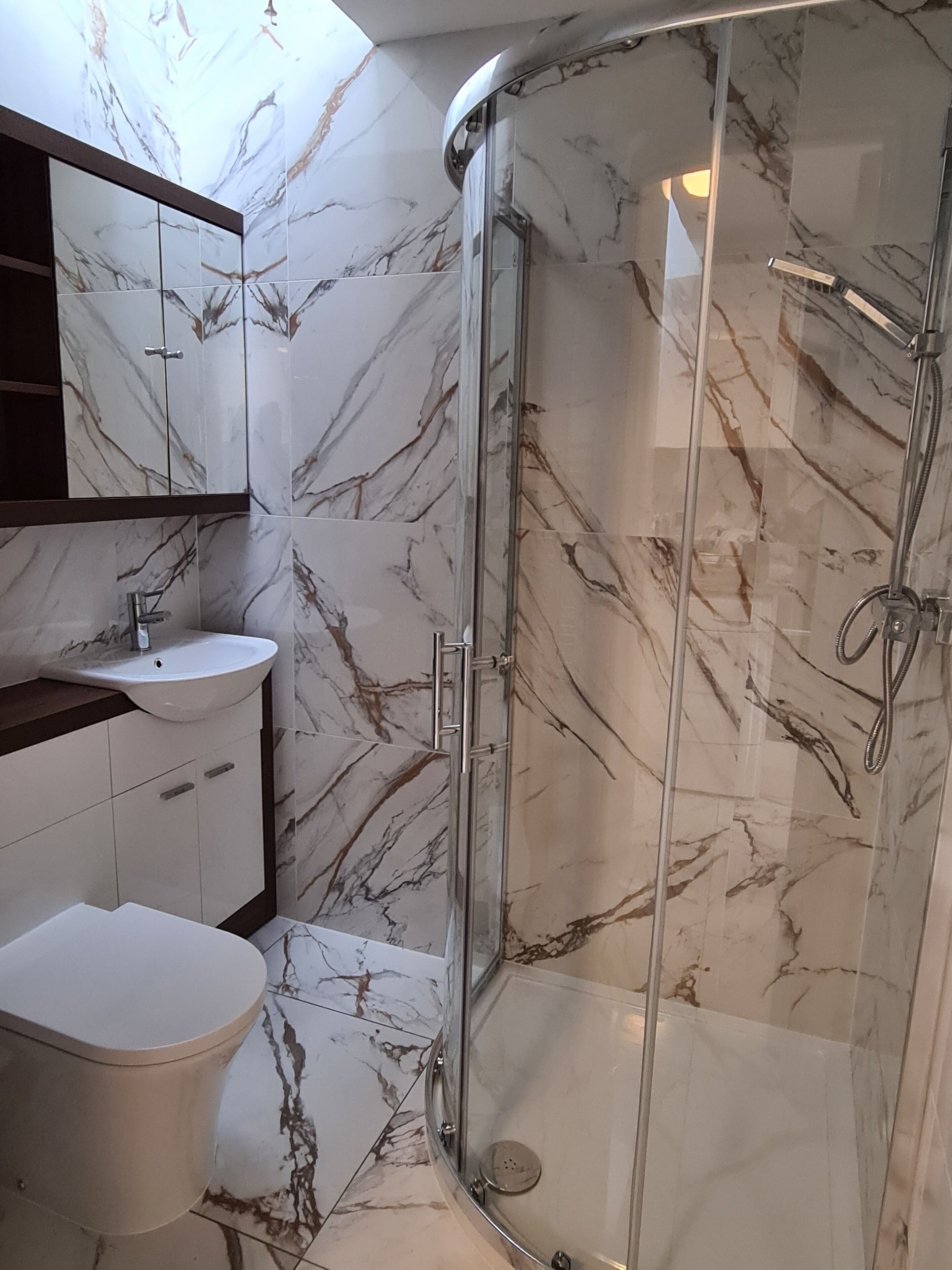 A bathroom with a glass-enclosed shower, a white sink, and a toilet.