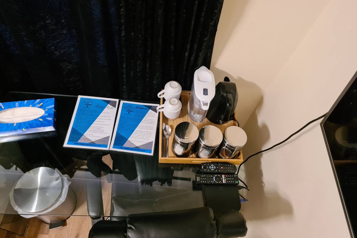 A room with a glass table displaying a menu, a kettle, a coffee maker, and a tray with cups and a bowl.
