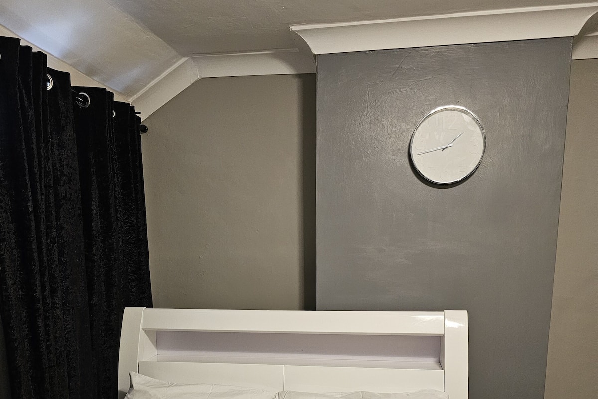 A neatly made bed with white bedding in a room with a grey wall and a white headboard.