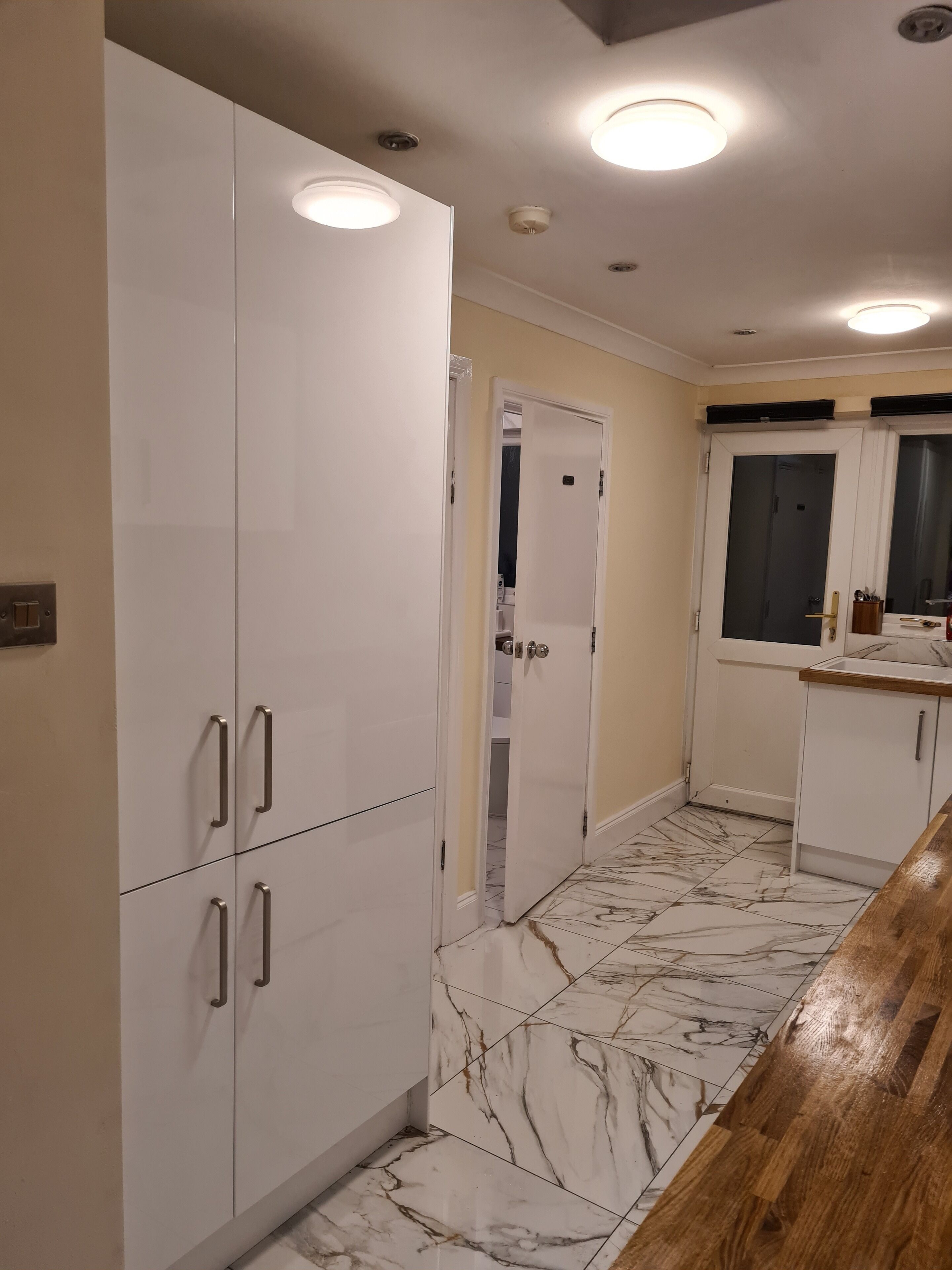 A kitchen with white cabinets, a marble-tiled floor, and a wooden countertop.