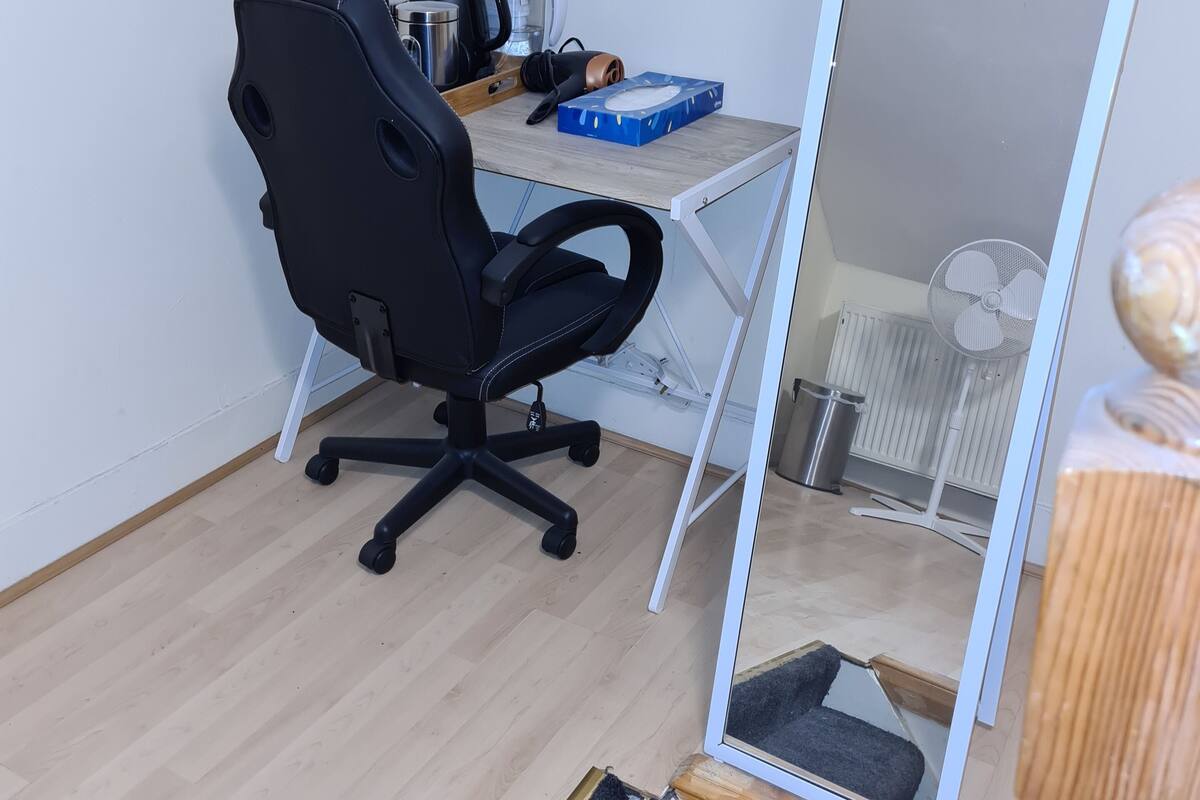 A small, compact room with a desk, a black office chair, a mirror, and a radiator.