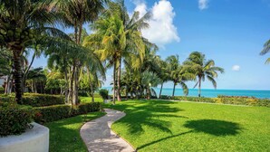 A paved pathway curving through a well-maintained grassy area with palm trees and a view of the ocean.