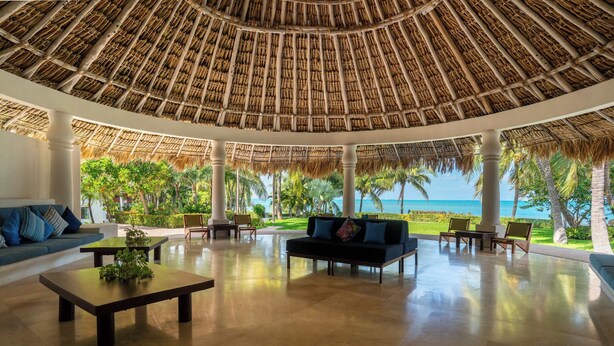 A spacious lounge area with a thatched roof, comfortable seating, and a view of the ocean.