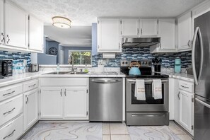 A modern kitchen with white cabinets, stainless steel appliances, and a blue tiled backsplash.