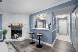 A living room with a stone fireplace, two bar stools, a rug, and a white-framed mirror. - Cozy End Unit Townhouse 1 Mile from Downtown Cary (Cary)