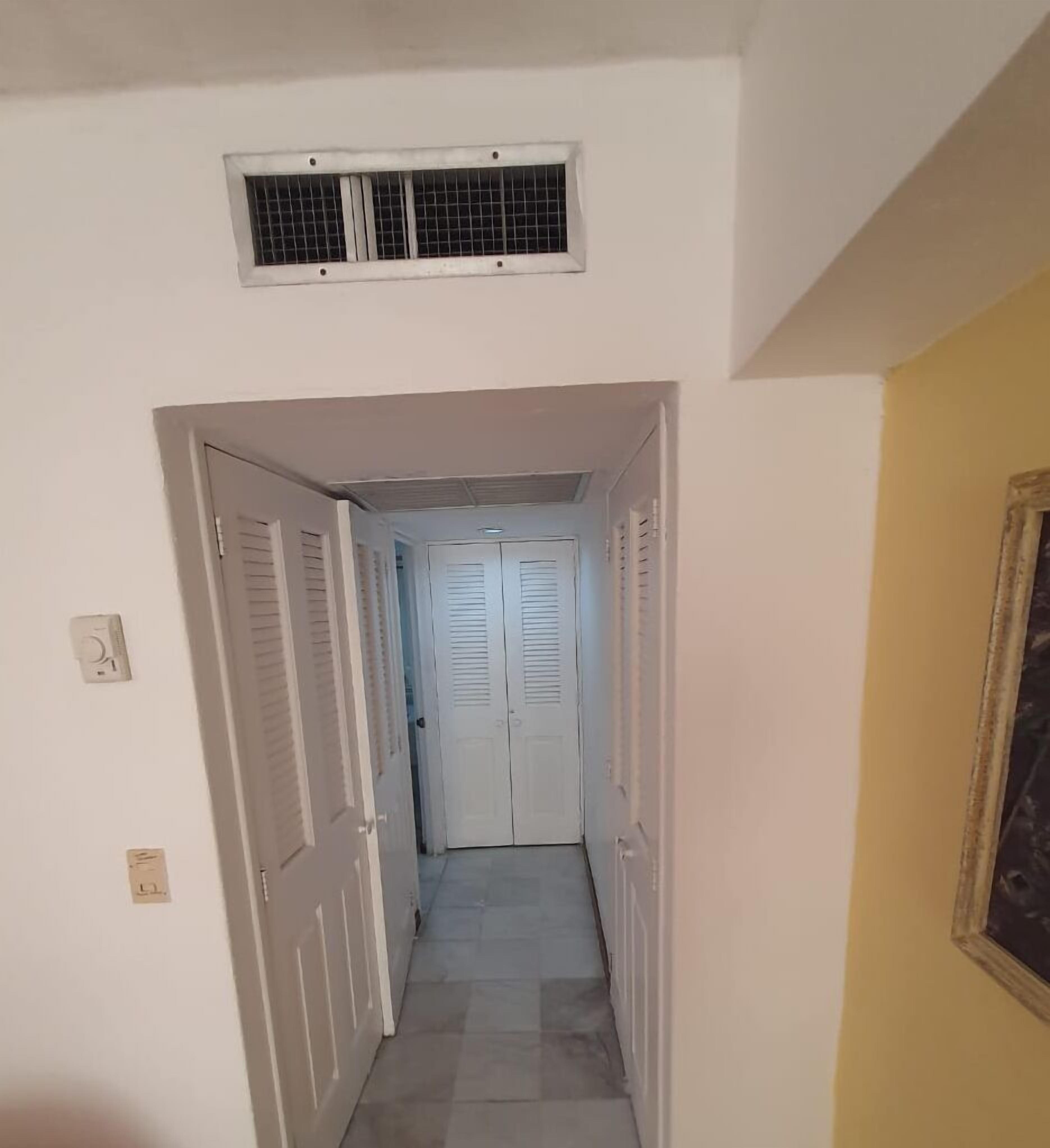 A narrow hallway with white doors and a vent above.