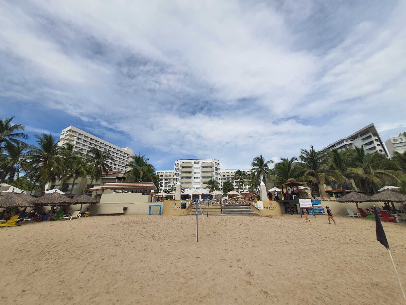 Een strand met palmbomen, een volleybalnet en een hotel op de achtergrond.
