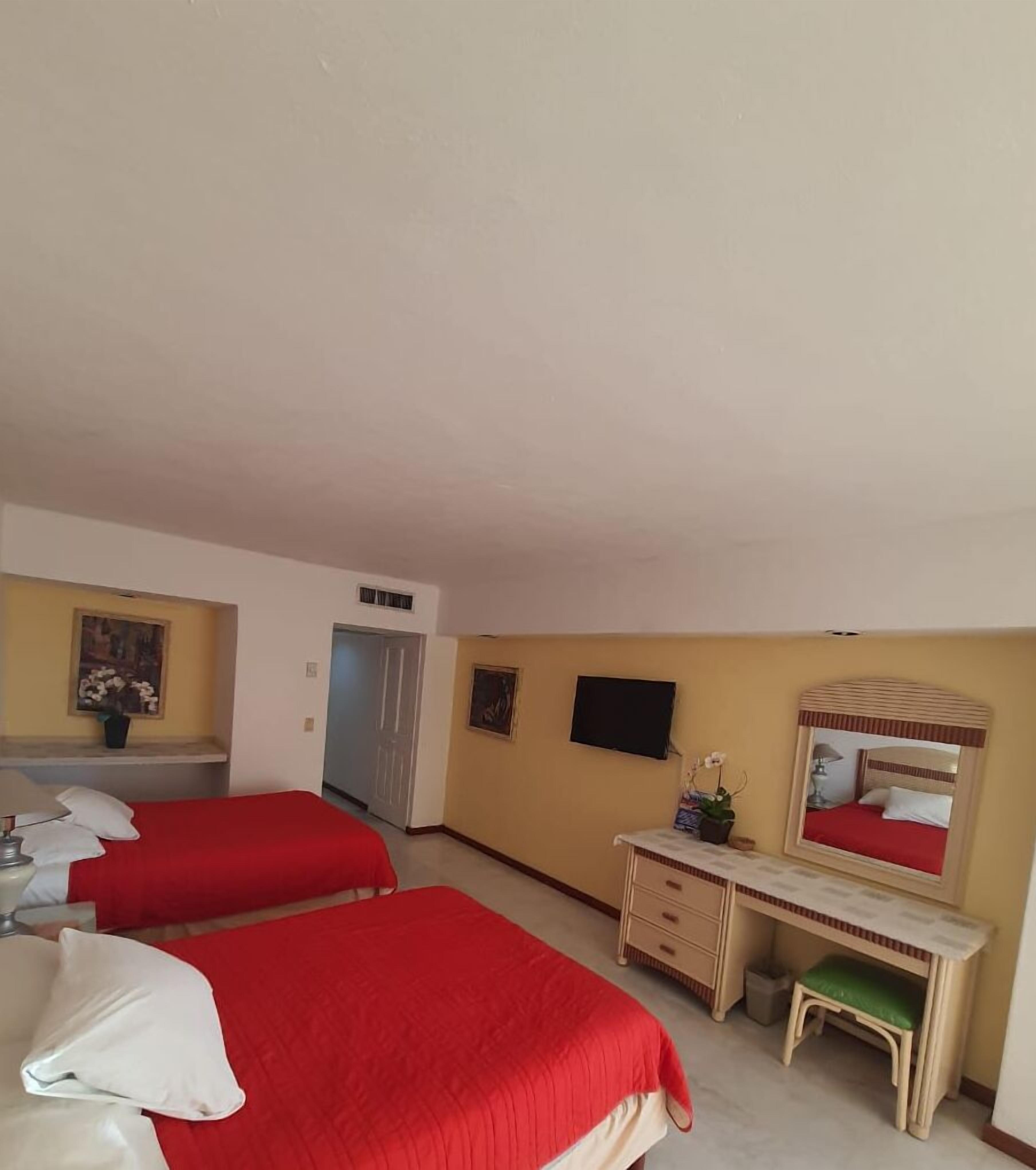 A hotel room with two single beds, a desk with a chair, a television, and a mirror.