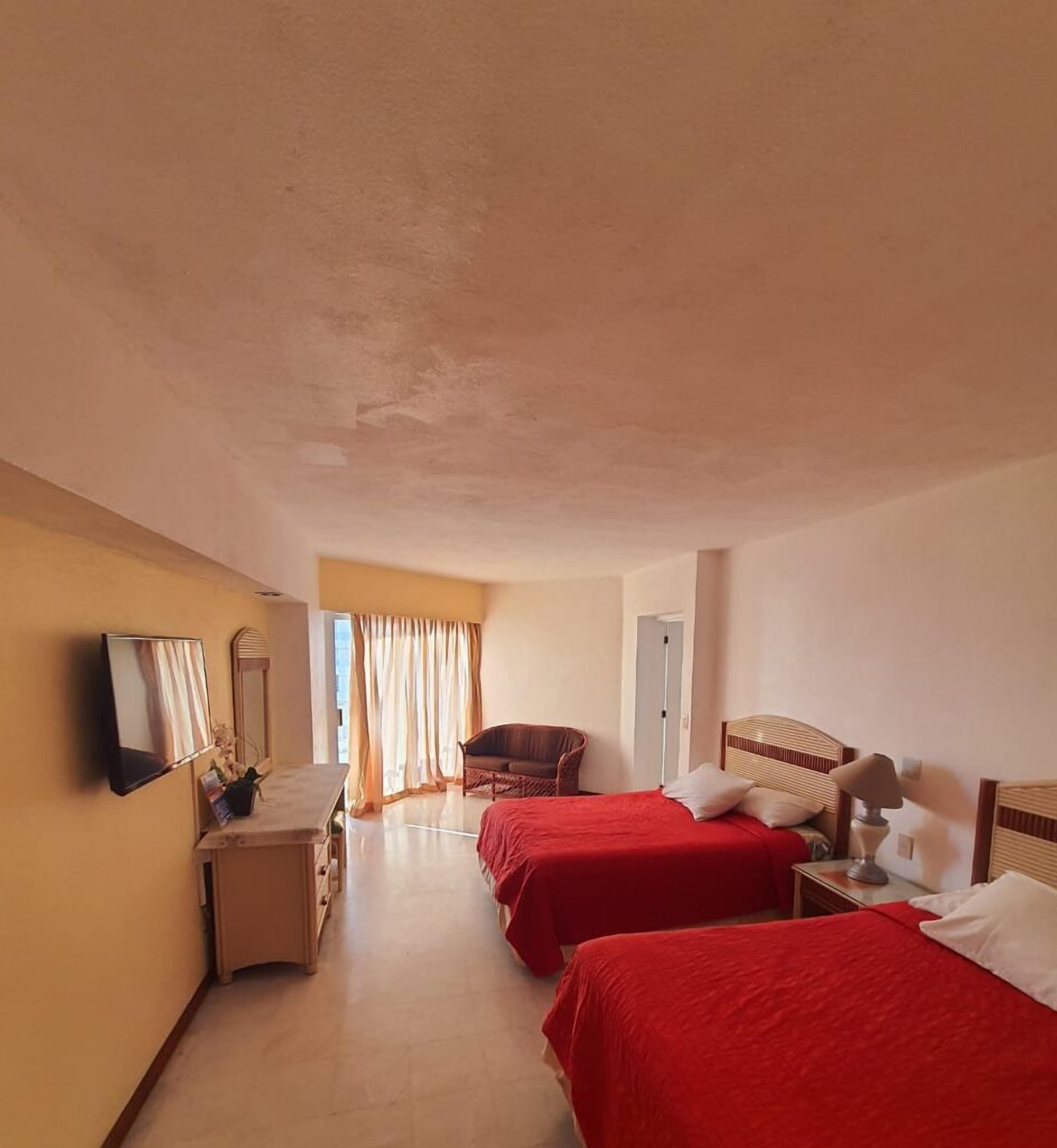 A hotel room with two beds, a chair, a desk, a mirror, and a window with curtains.