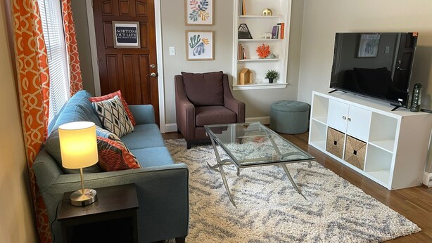 A living room with a sofa, armchair, glass coffee table, TV stand, and decorative items. - Delightful house just 10 minutes from uptown (Charlotte)