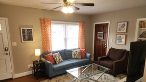 A living room with a blue sofa, a glass coffee table, a brown armchair, a ceiling fan, and a door labeled "SORTING OUT LIFE". - Delightful house just 10 minutes from uptown (Charlotte)