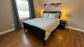 A bedroom with a bed, two bedside tables with lamps, a window with curtains, and a painting on the wall. - Delightful house just 10 minutes from uptown (Charlotte)