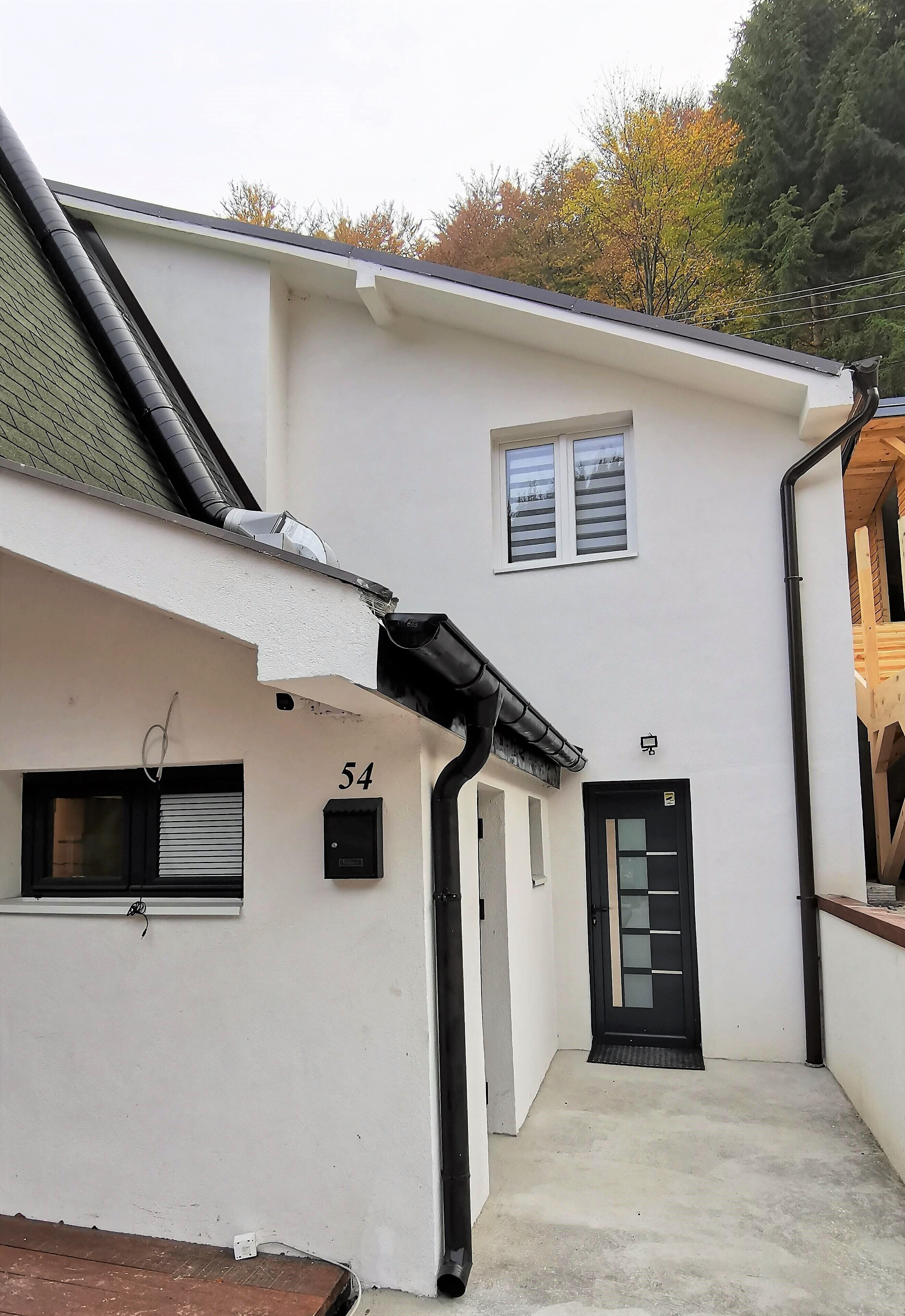 A white building with a black door and window, number 54, and a small window with a shutter.