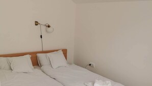 Un lit double avec une literie et des serviettes blanches, une tête de lit en bois et une lampe fixée au mur.