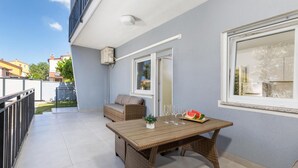A balcony with a wicker table, a sofa, and a window with a view of the neighborhood.