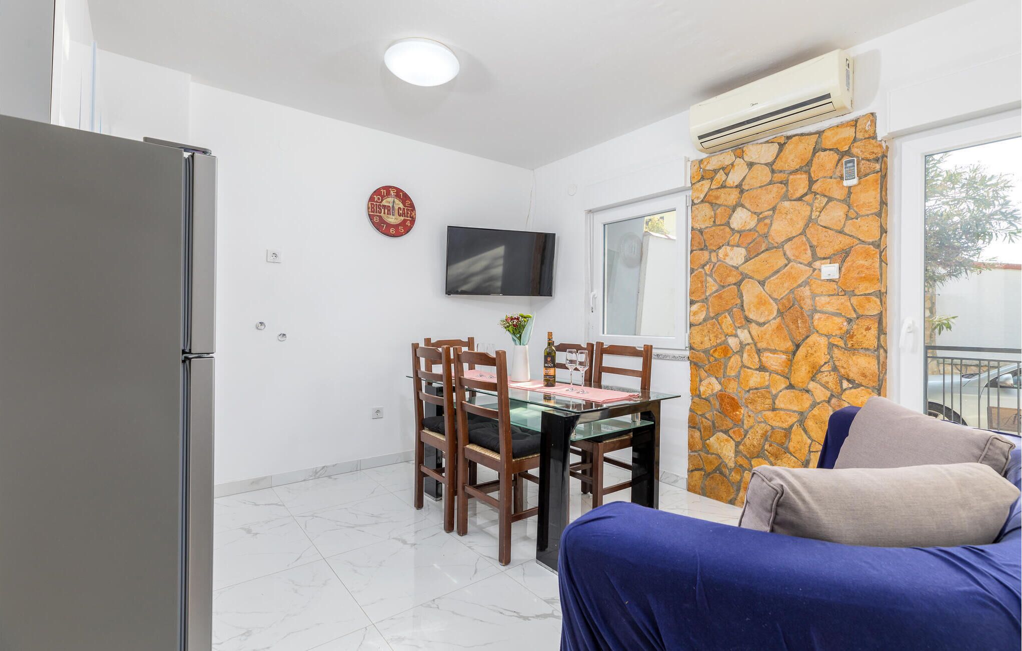 A compact living space with a dining area, a TV mounted on the wall, a stone wall, and a balcony with a view.