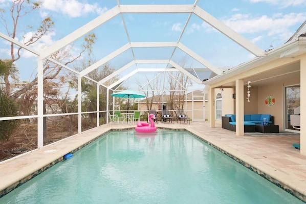 A covered swimming pool with a pink flamingo float, a green umbrella, and outdoor seating.