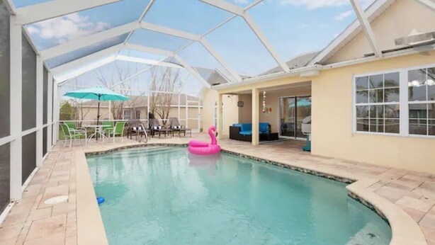 Ein überdachter Pool mit einem rosa Flamingo-Schwimmspielzeug, eine Terrasse mit Stühlen und Blick ins Freie.