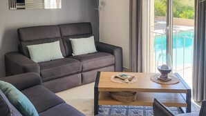 Un salon avec un canapé, une table basse et une vue sur une piscine, visible à travers de grandes fenêtres.