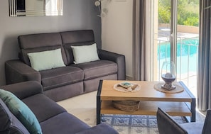 Een woonkamer met een bank, een salontafel en uitzicht op een zwembad door grote ramen.