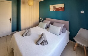 Een net opgemaakt bed met opgerolde handdoeken, een enkele stoel en een schilderij aan de muur.