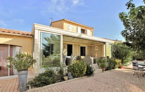 Une maison moderne à deux étages, dotée d’une façade en verre, d’un espace extérieur aménagé et de plantes en pot.