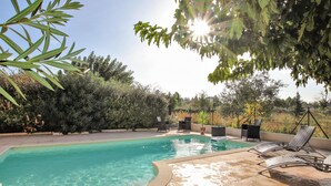 Une piscine à bords incurvés, entourée d’un patio aménagé avec des chaises et une table.