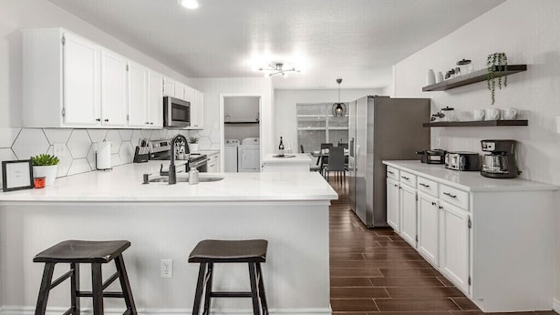 A modern kitchen with white cabinets, a central island, and a dining area in the background. - Contemporary home in the heart of McKinney (McKinney)