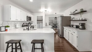 A modern kitchen with white cabinets, a central island, and a dining area in the background. - Contemporary home in the heart of McKinney (McKinney)