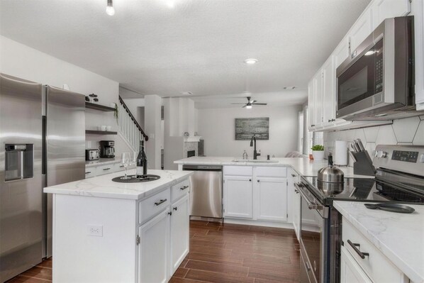 A modern kitchen with stainless steel appliances, white cabinetry, and a marble countertop.