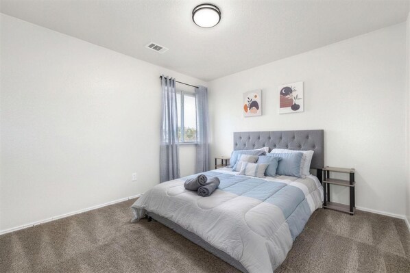 A bedroom with a bed, a nightstand, a window with curtains, and two wall art pieces.