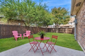 A backyard with a red metal table and chairs, a potted plant, and a wooden fence.