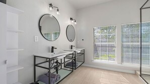 A modern bathroom with two sinks, a large mirror, and a window with blinds. - Contemporary home in the heart of McKinney (McKinney)