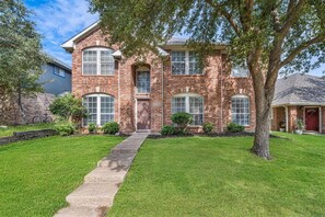 A two-story brick house with a front porch, a driveway, and a well-maintained lawn.
