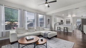 A modern living room with a sectional sofa, a coffee table, and a view of the backyard through large windows. - Contemporary home in the heart of McKinney (McKinney)
