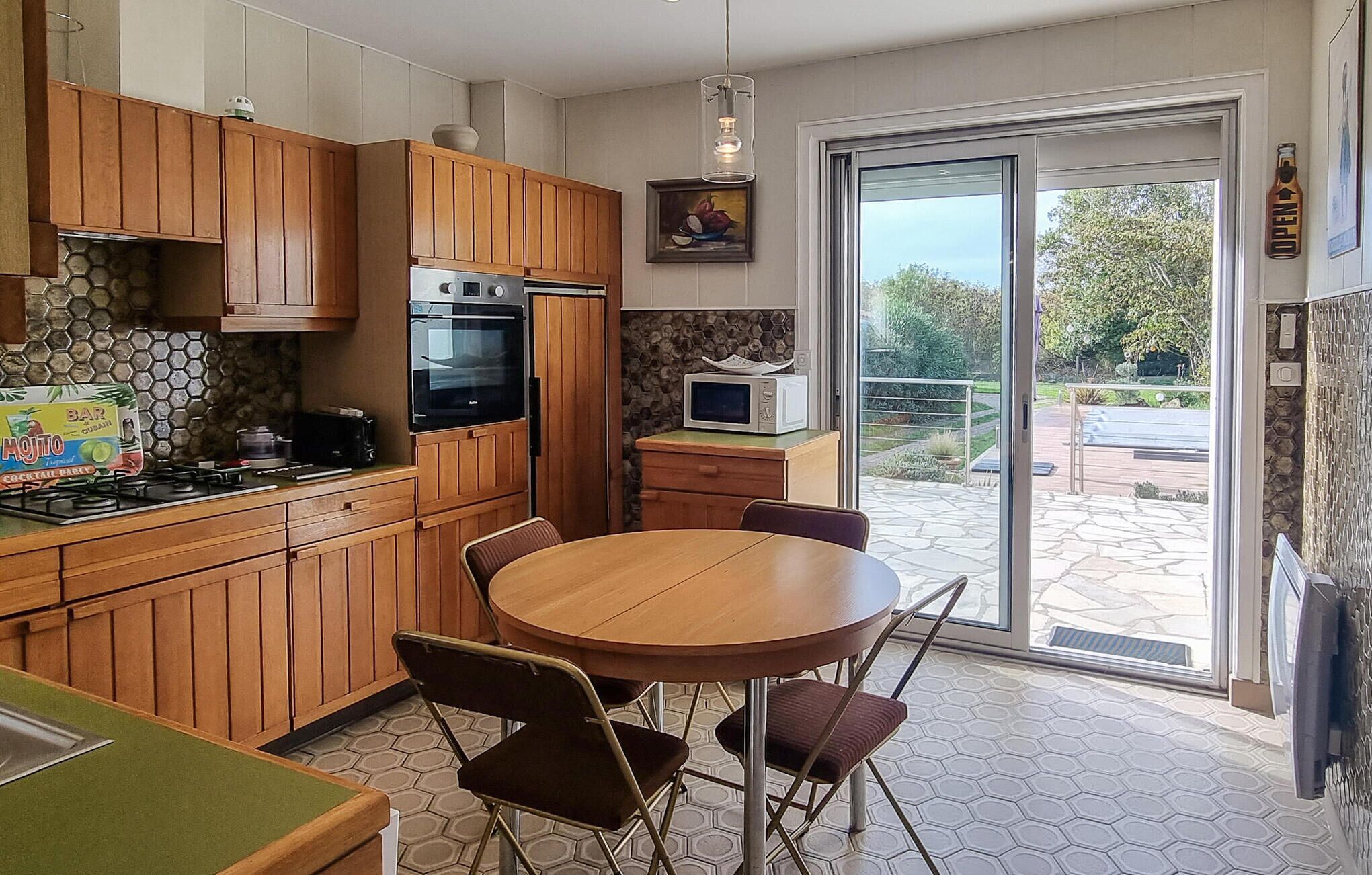 A kitchen with wooden cabinets, a round dining table, and chairs. There is a microwave on the counter, and a window with a view of the outdoors.