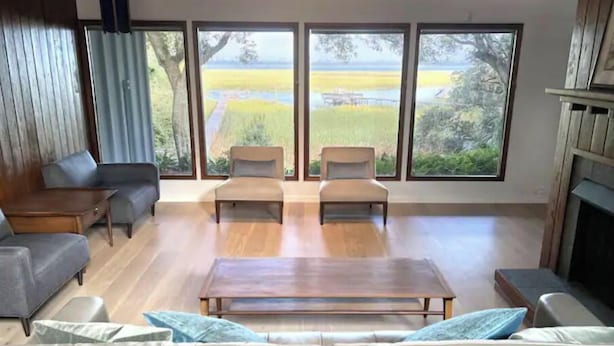 A spacious living room with a large window, a sofa, two armchairs, and a coffee table. - MCM Magic on the Marsh (Mount Pleasant)