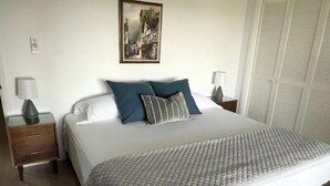 A neatly made bed with a patterned bedspread, two pillows, and a bedside table with a lamp. - MCM Magic on the Marsh (Mount Pleasant)