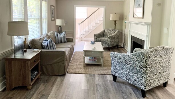 A living room with a sofa, armchair, coffee table, and lamps. There is a fireplace and a staircase in the background.