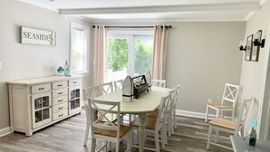 A dining area with a white table and chairs, a cabinet with drawers, and a sign reading "SEASIDE".