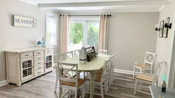 Un coin repas avec une table et des chaises blanches, un meuble avec des tiroirs et une enseigne indiquant « AU BORD DE LA MER ».