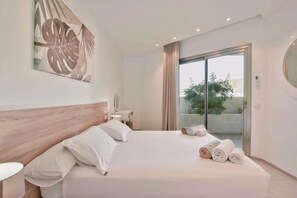 A hotel room with a large bed, a wooden headboard, a bedside table, a mirror, and a view of the outdoors through a sliding glass door.
