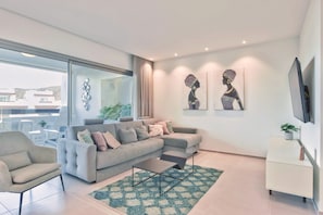 Ein modernes Wohnzimmer mit grauem Sofa, einem Couchtisch, einem Fernseher und Kunstwerken an der Wand.