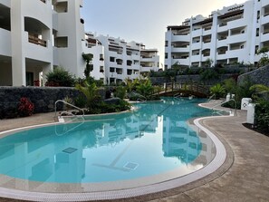 A swimming pool surrounded by a landscaped area with a stone wall and greenery.
