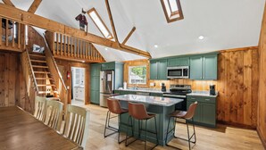 Una cocina moderna con armarios de madera, una isla central con taburetes altos y una escalera que lleva a un nivel superior.