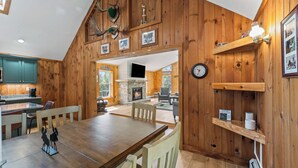 A wooden interior with a dining area, kitchen, and fireplace.