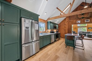 A modern kitchen with green cabinets, stainless steel appliances, and a wooden ceiling.