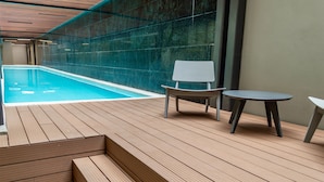A wooden deck with a pool, a chair, and a table.